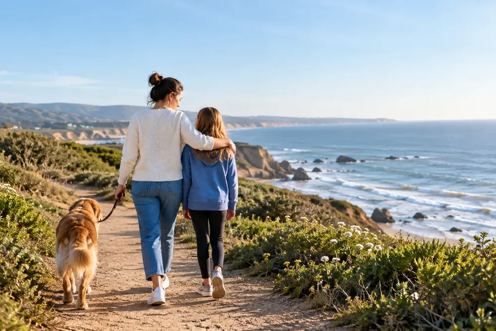 An adult and child walking a dog along a quiet coastal path
