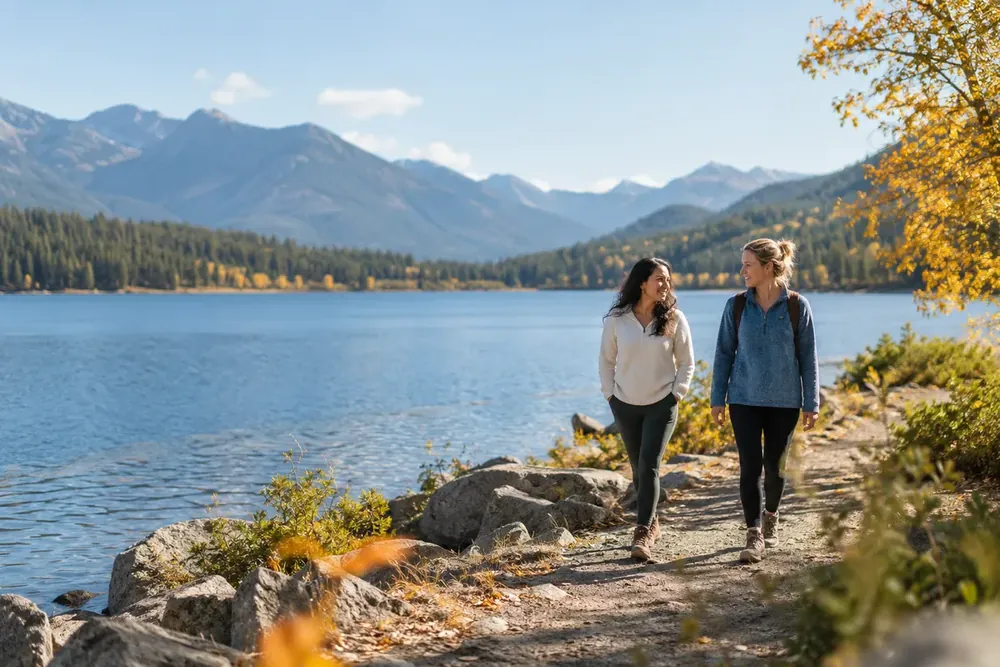 Two women walking together beside a calm lake.