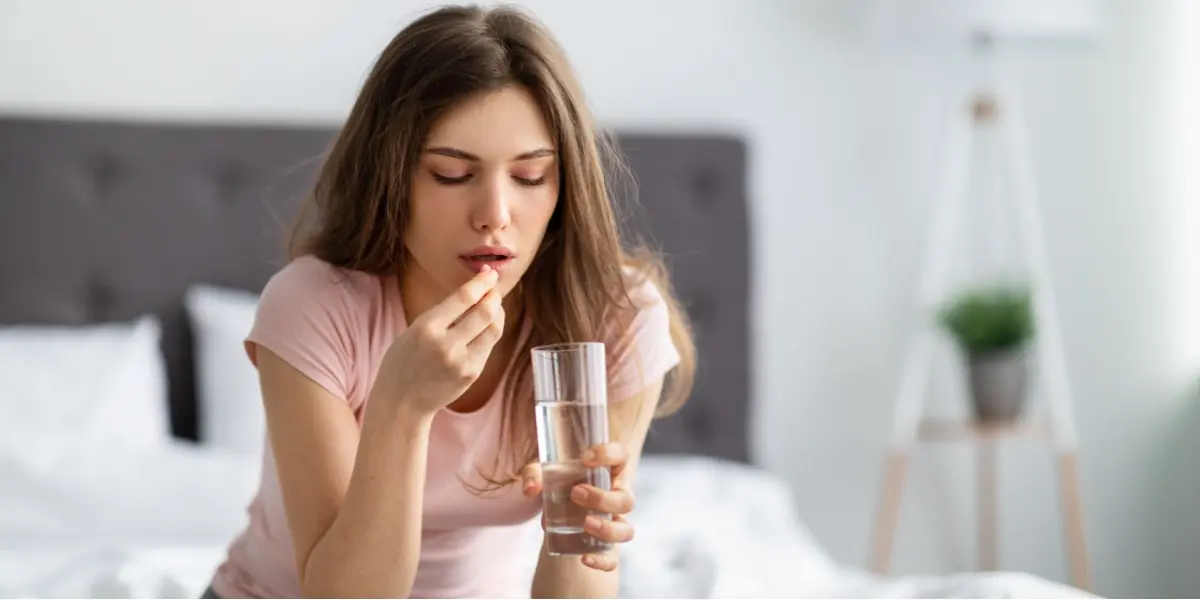 A woman holds a glass of water and a tablet.