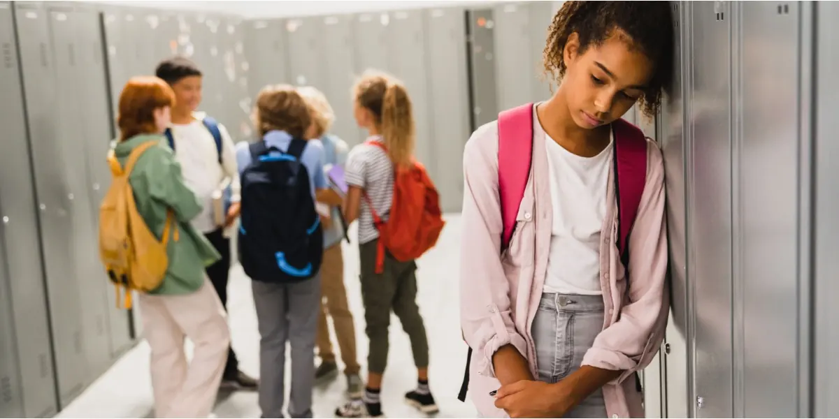 A student stands apart from a group in a school corridor.
