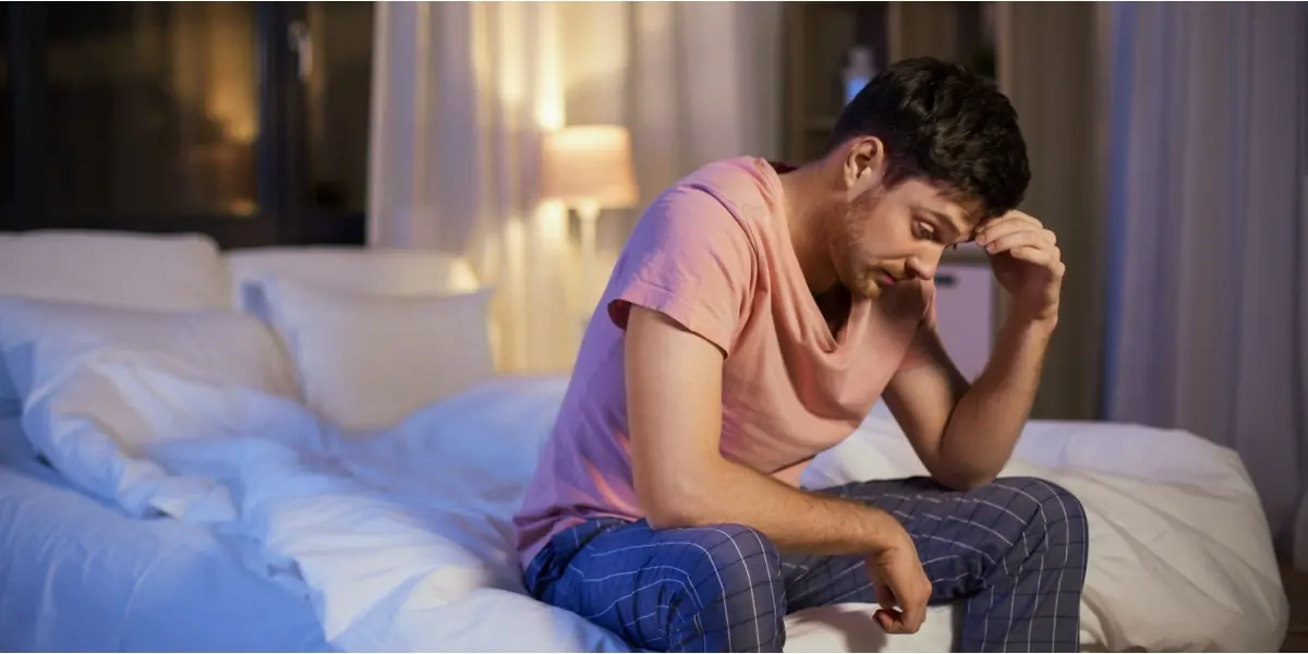 A man sits awake at the edge of a bed.