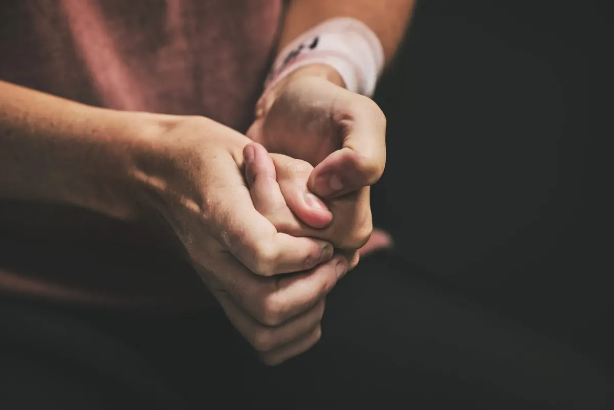 A seated person rests their clasped hands on their lap.