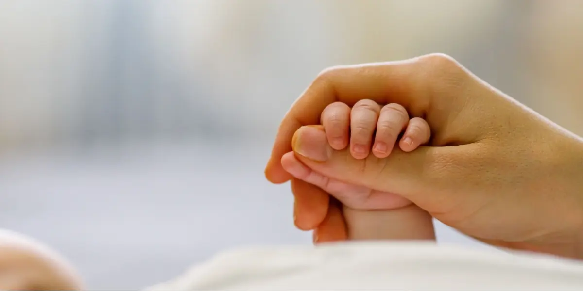 An infant holds an adult’s finger.