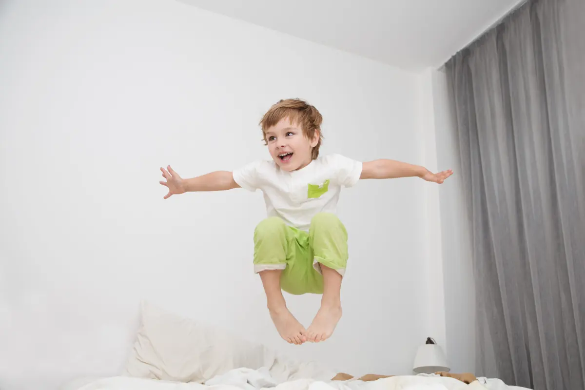 A child plays energetically on a sofa at home.