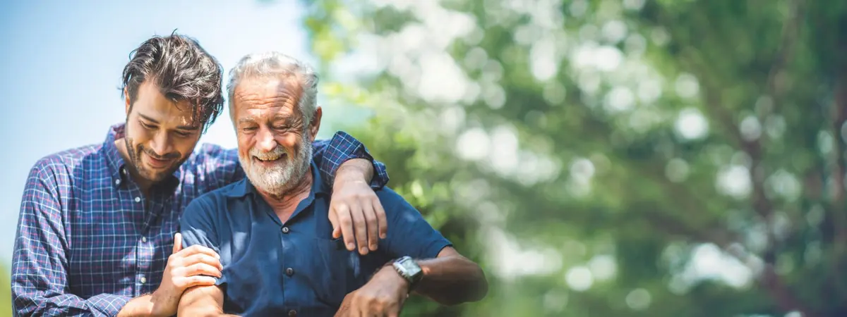 Two men of different generations smile together outdoors.