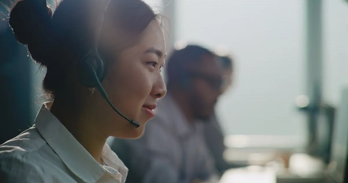 A support worker wearing a headset listens at a desk.