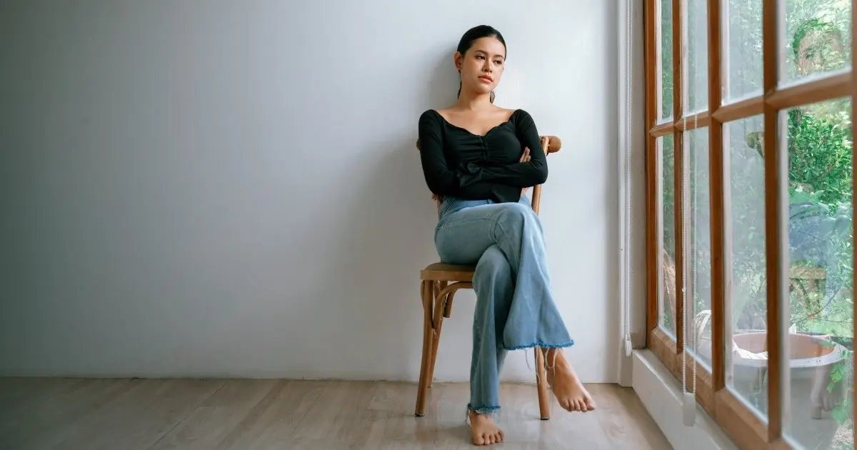 A woman sits beside a bright window in a quiet room.