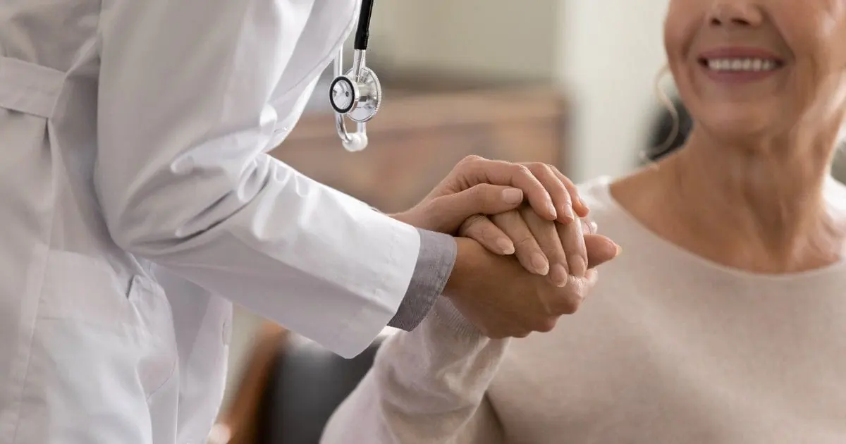 A healthcare professional offers a reassuring hand to an older adult.