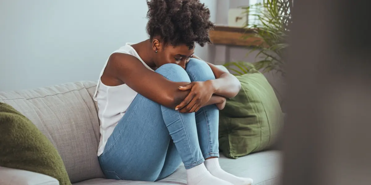A young person sits quietly with their arms around their knees.