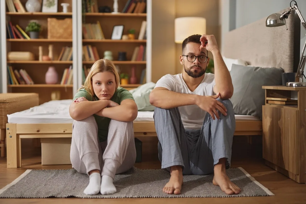 A father and child sit together on the floor at home.