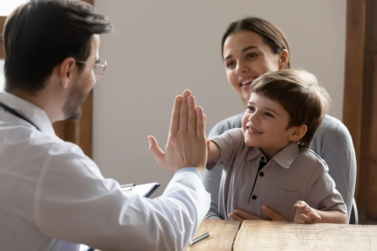 A doctor speaks with a parent and child during a consultation.
