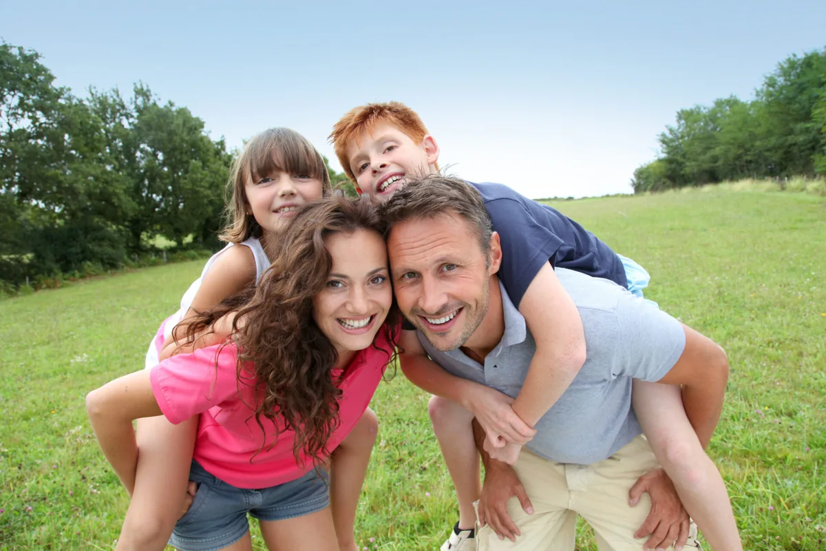 A family enjoys a playful piggyback ride in a green park.