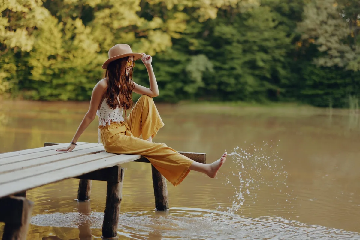 A woman relaxes beside a lake beneath green trees.
