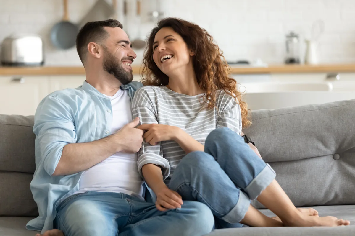 A couple talks and smiles together on a sofa.
