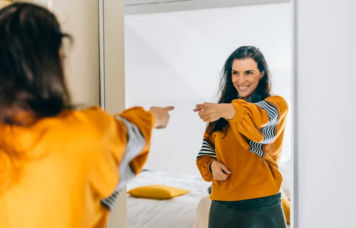 A woman makes a playful face at her reflection in a mirror.