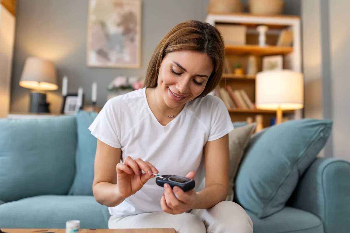 A woman checks her blood glucose while sitting at home.