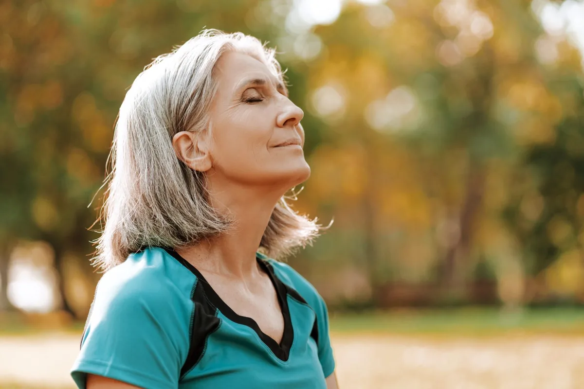 An older woman closes her eyes in an autumn park.