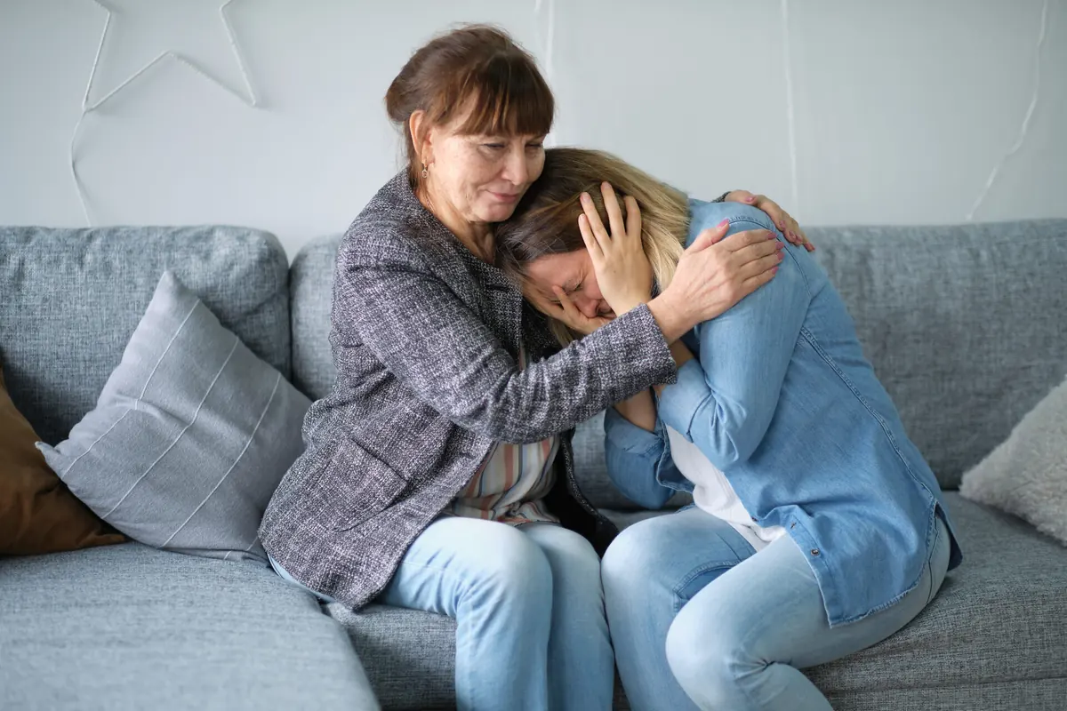 Two adults comfort one another while sitting on a sofa.