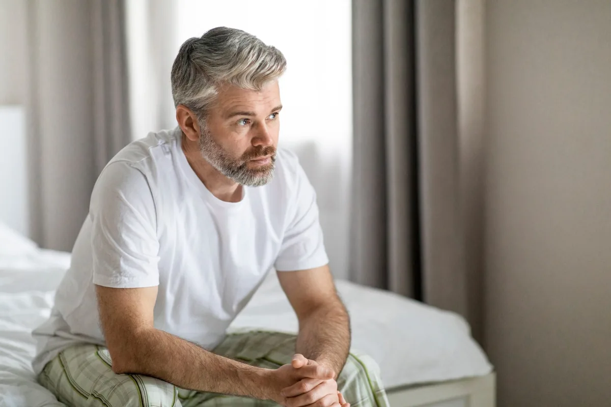 An older man sits quietly beside a window.