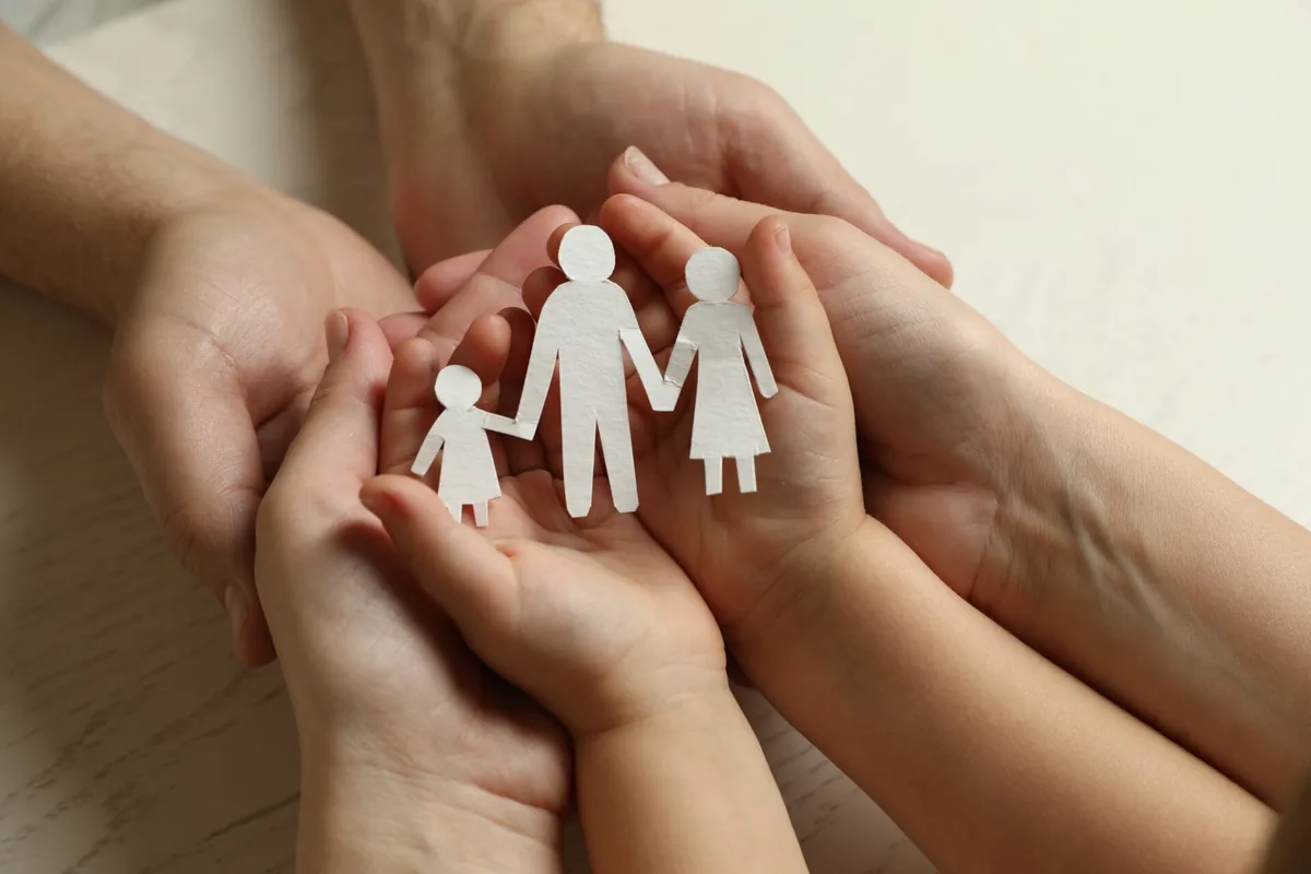 Hands cradle small paper figures representing a family.