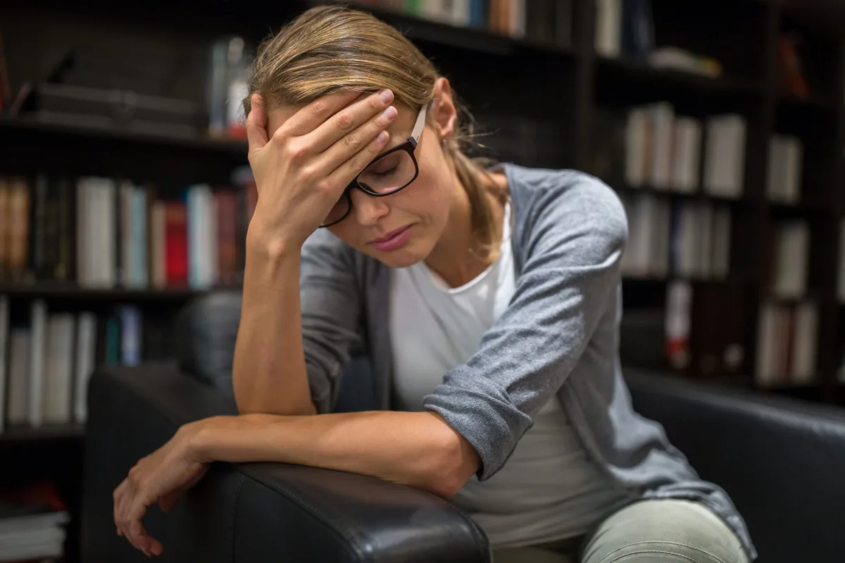 A woman takes a break from work with one hand resting on her forehead.