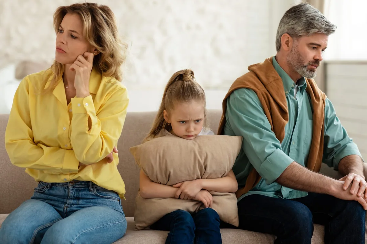 Parents and a child sit together thoughtfully on a sofa.