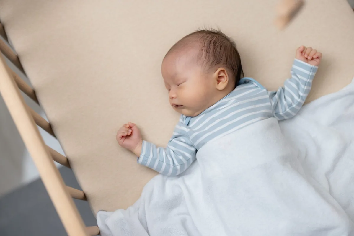 A baby sleeps on their back in a clear cot.