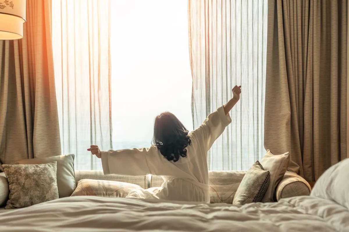 A person stretches their arms toward the sunlight from a sofa.
