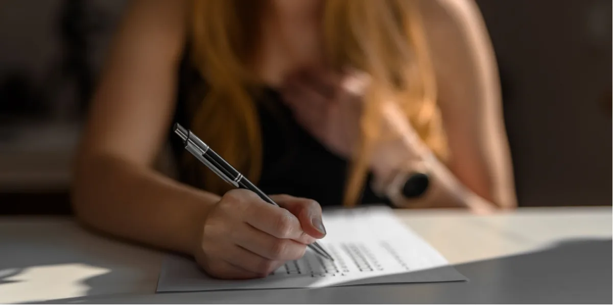 A woman writes in a notebook at a desk.
