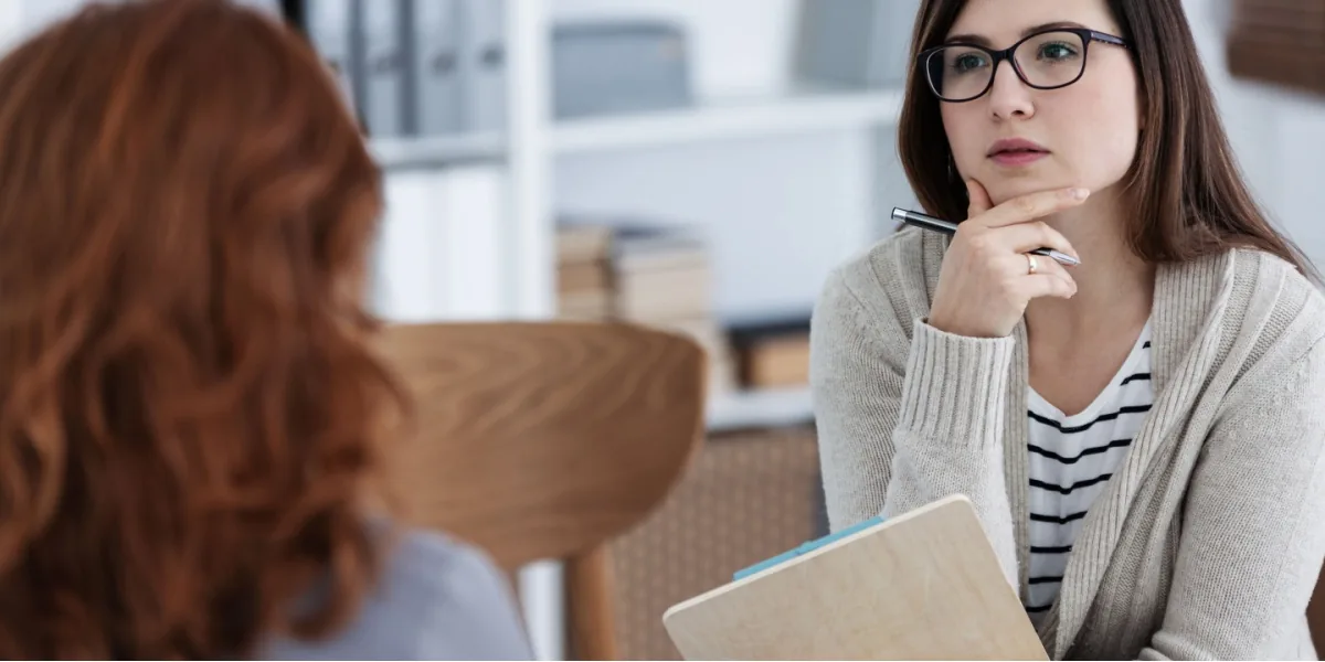 A woman listens thoughtfully to another person in a counseling room.