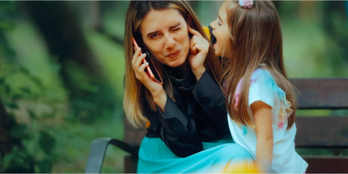 A parent leans close to speak with a child on a park bench.