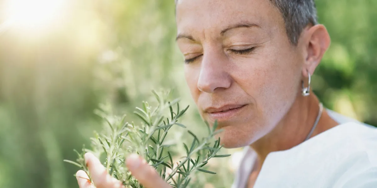A woman smells a sprig of fresh herbs outdoors.