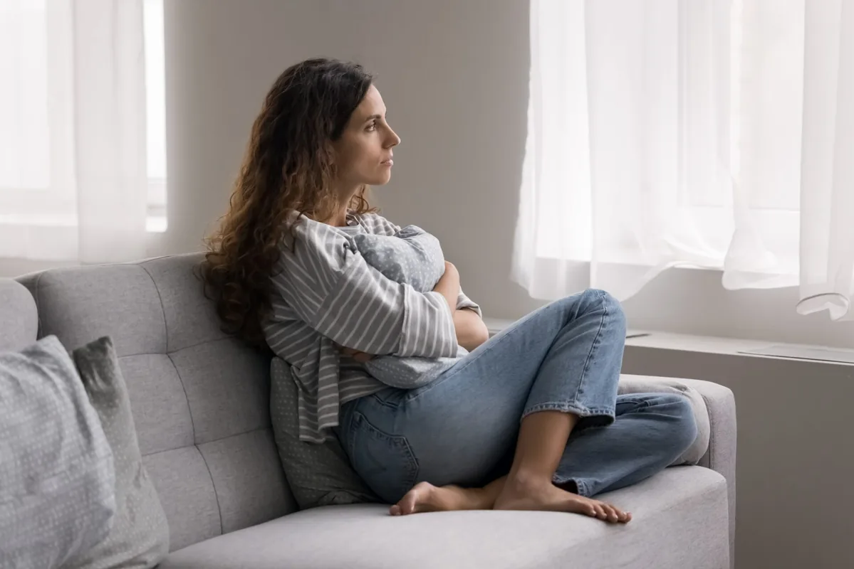 A woman takes a quiet moment seated beside a window.