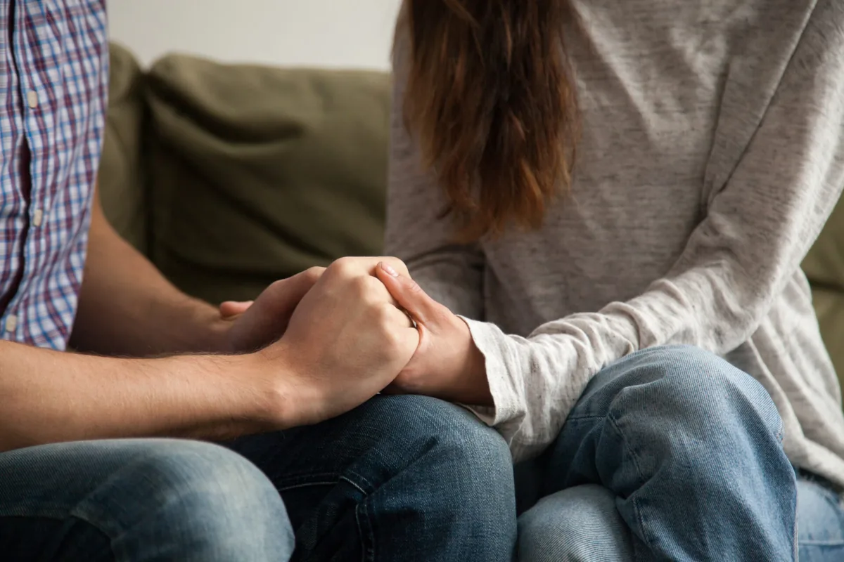 One person holds another person's hand during a quiet conversation.