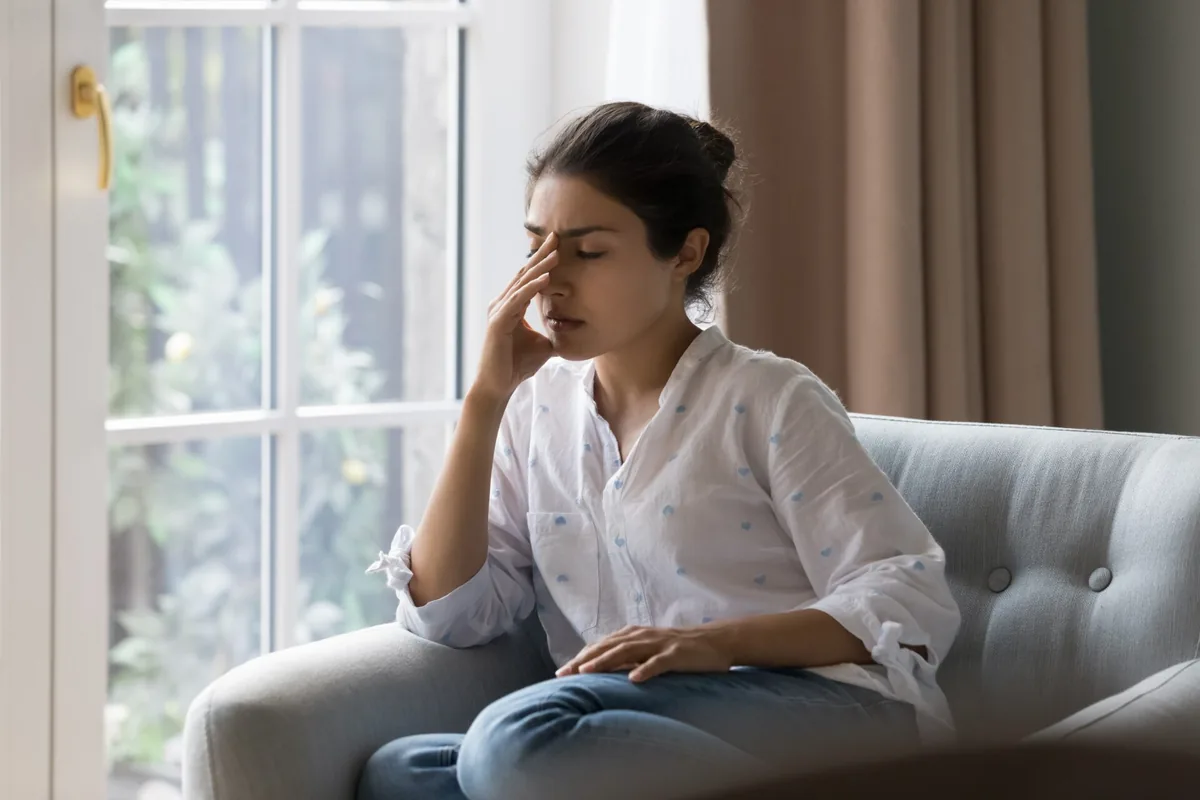 A woman takes a thoughtful pause during a conversation in a bright room.