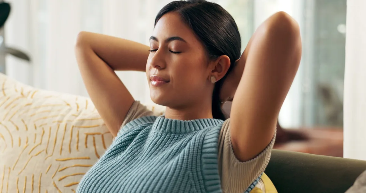 A woman closes her eyes while resting comfortably on a sofa.