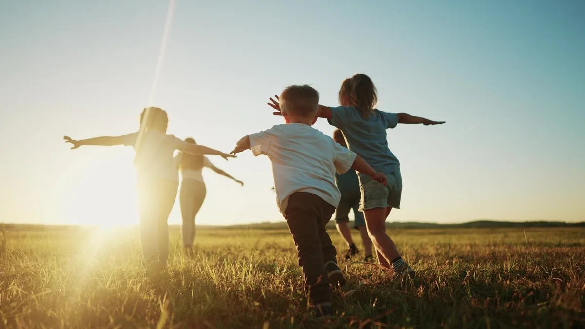 Children run together in an open field at sunset.