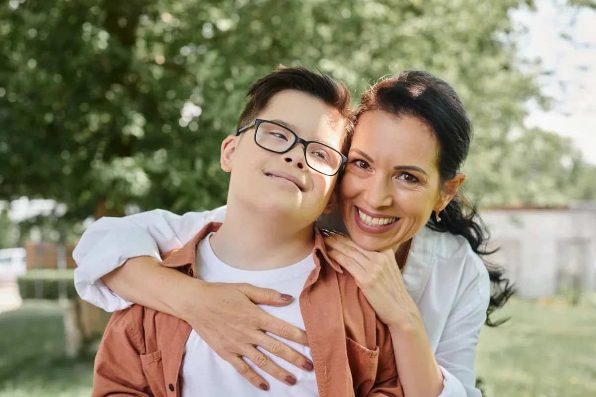 A young adult and a family member embrace and smile outdoors.