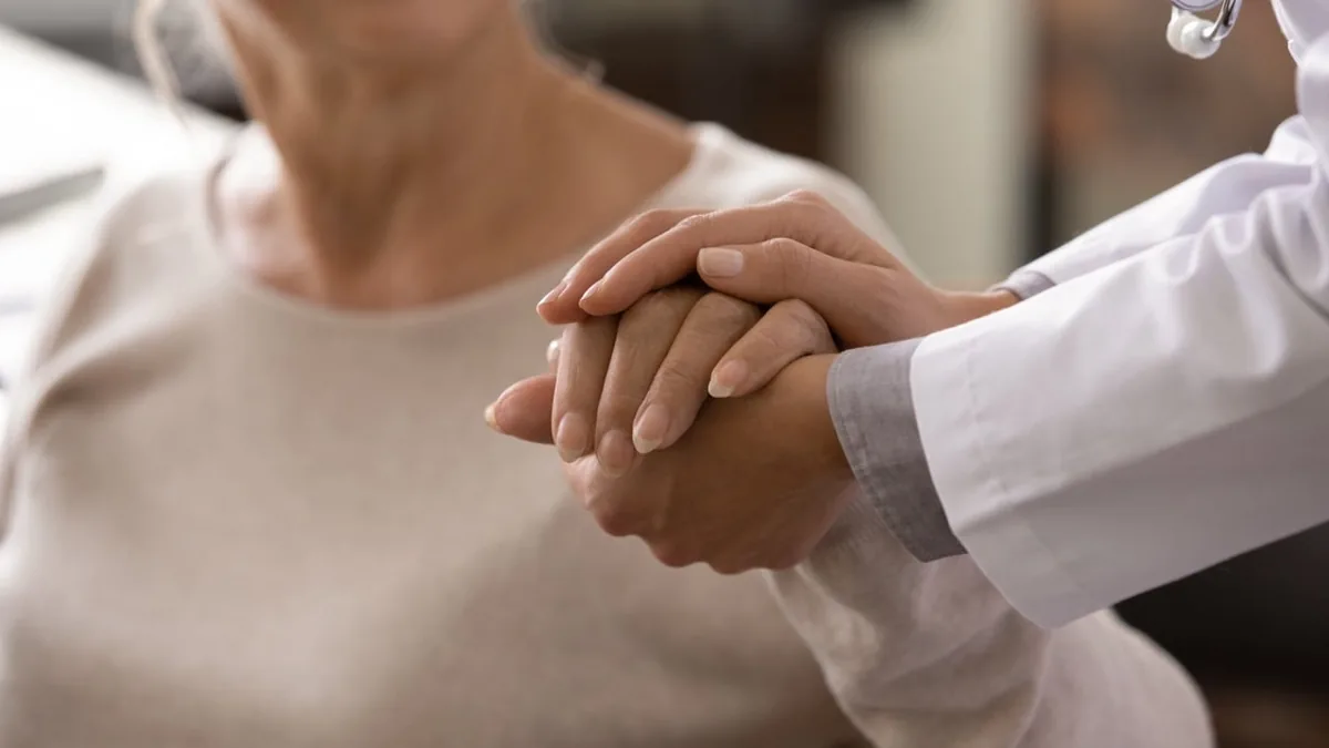 A healthcare professional gently supports an older adult's hands.