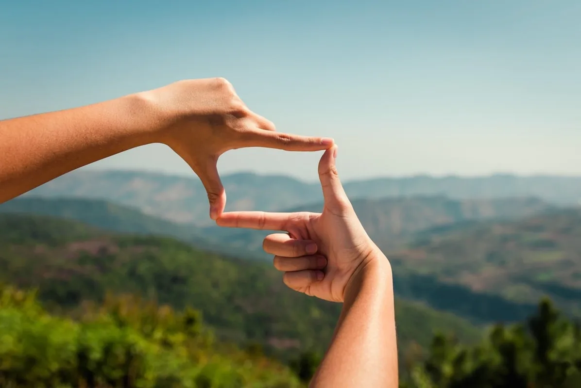 A person frames a distant mountain landscape with their hands.