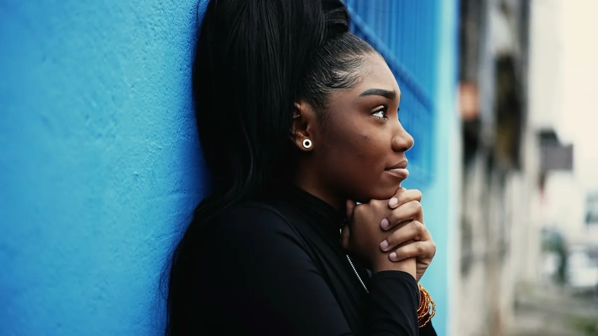 A woman takes a quiet pause beside a window in a bright room.