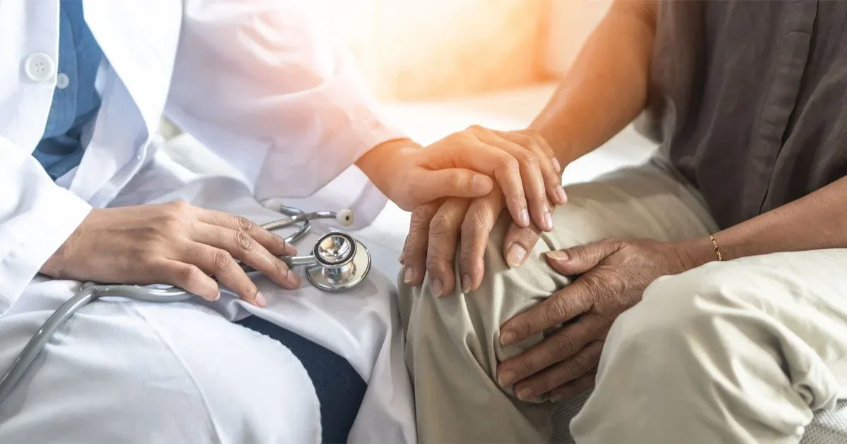 A healthcare professional rests a reassuring hand on a patient's knee.