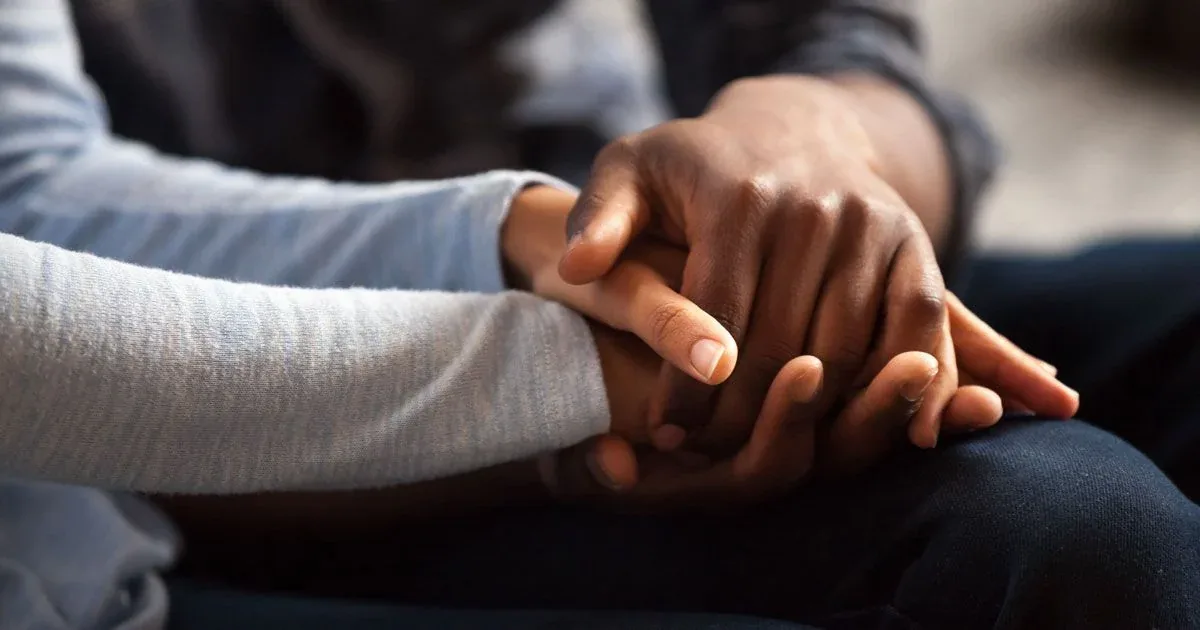 Two people hold hands during a supportive conversation.