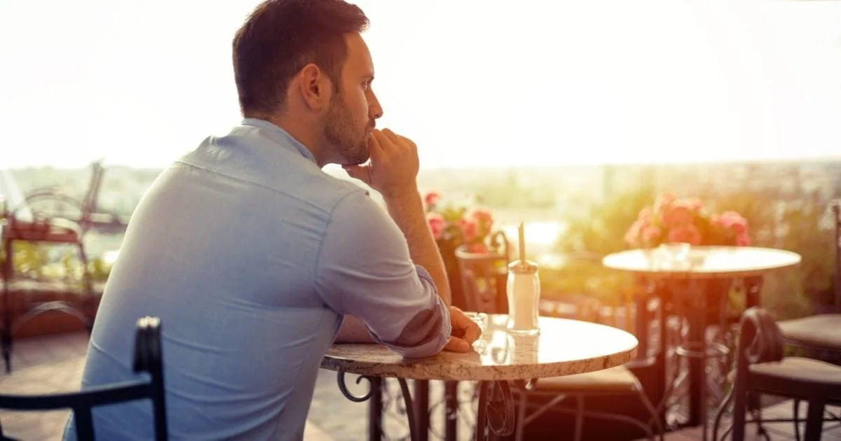 A man sits thoughtfully at an outdoor cafe as the sun sets.