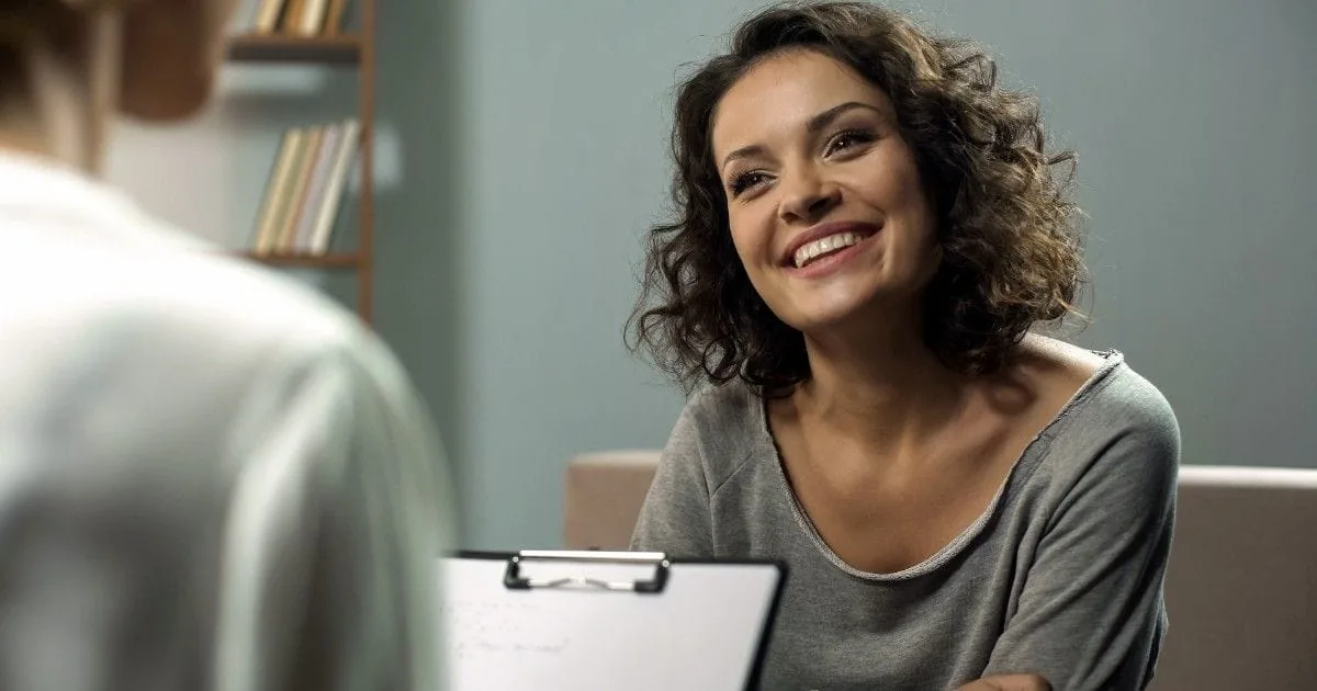 A woman smiles as she listens to another person during a conversation.