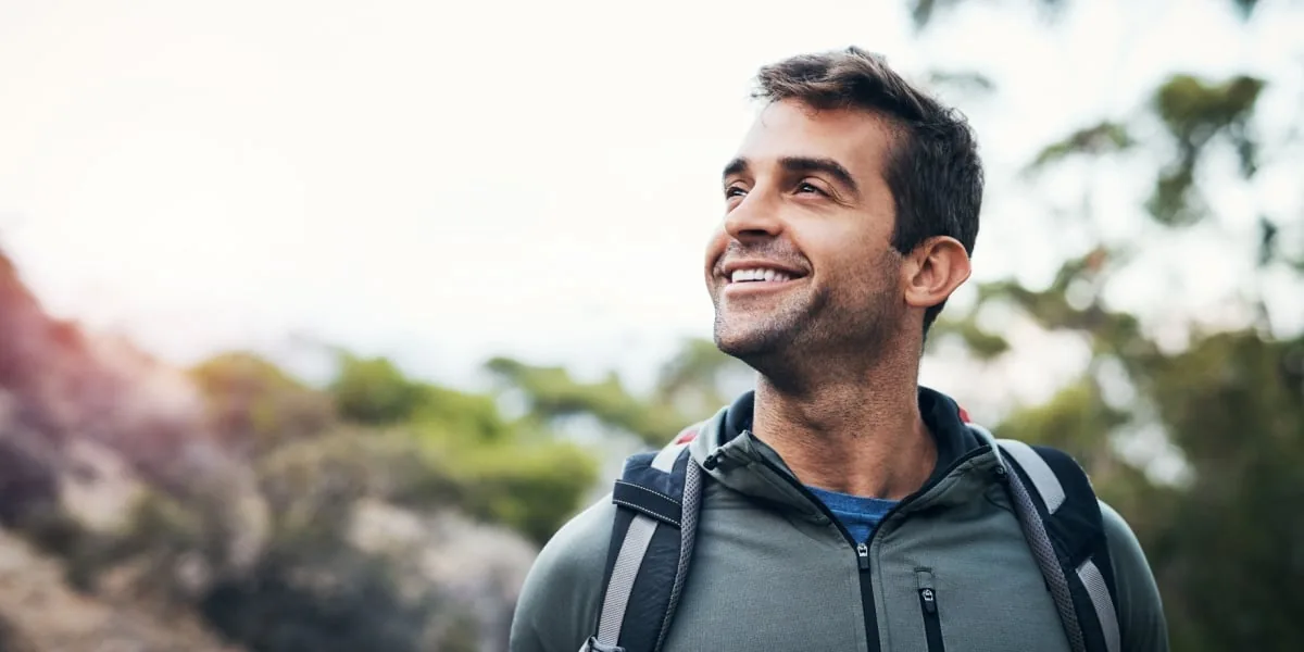 A man wearing a backpack smiles while walking outdoors.