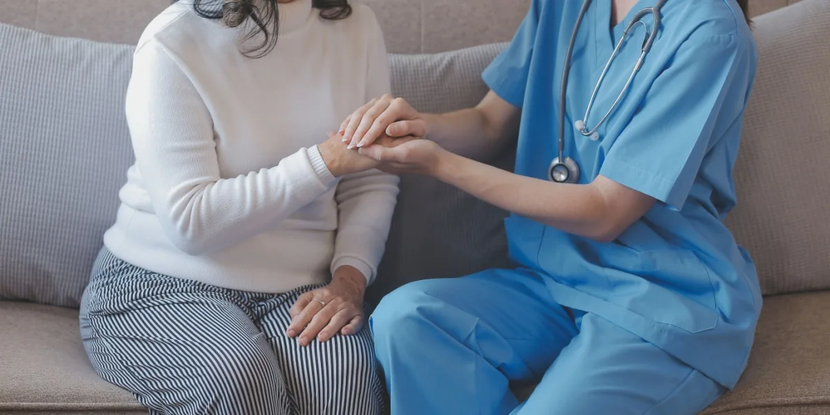 A healthcare worker supports an older person in a bright room.