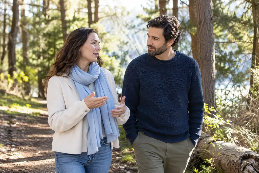 Two adults listen and talk on a woodland walk.