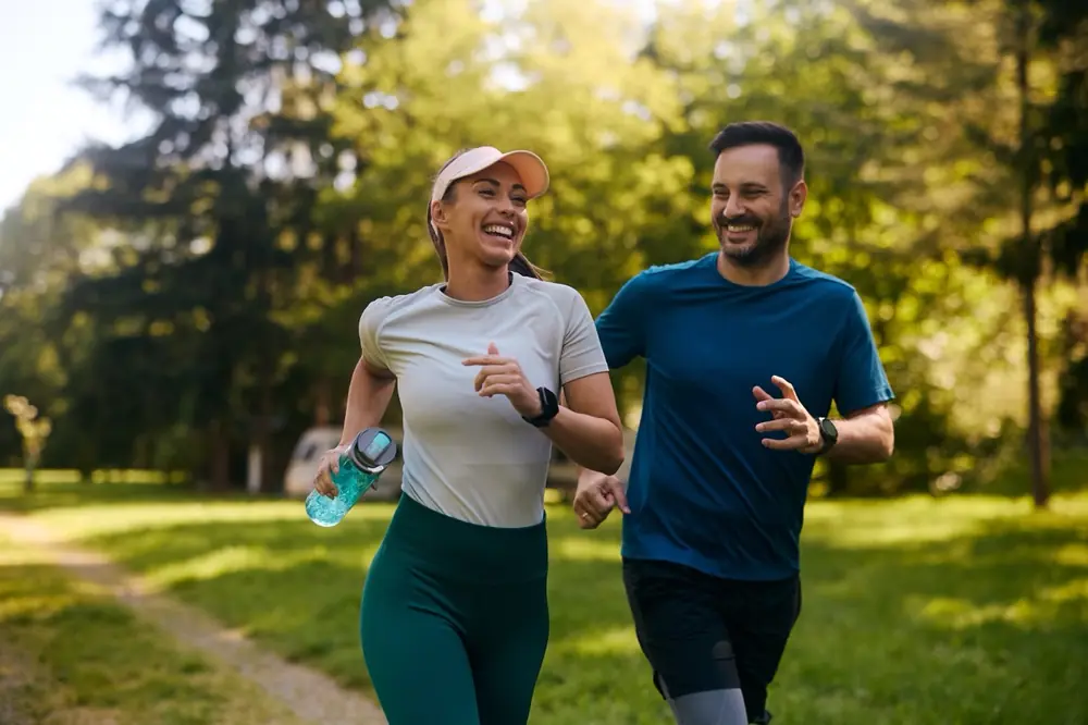 Two people go for a run together in a sunlit park.
