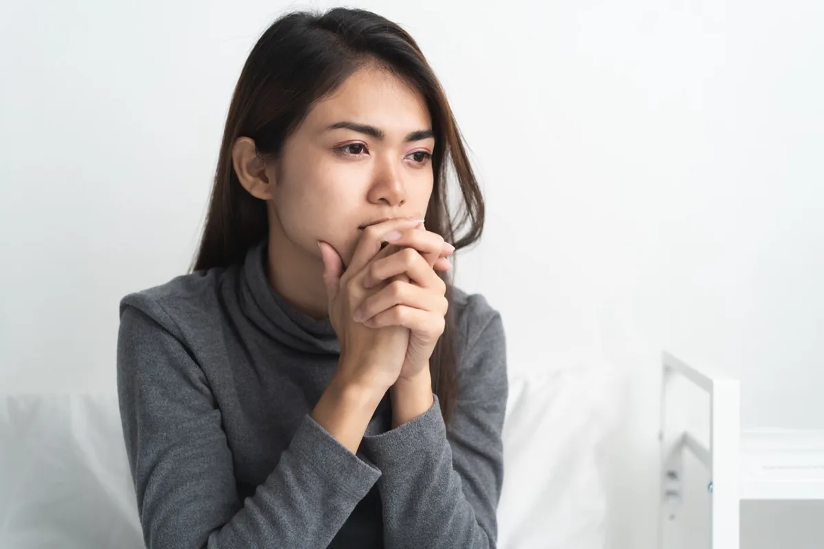 A woman pauses with her hands clasped near her chin.